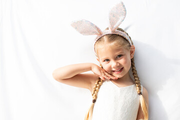 a portrait of a Beautiful blond blue-eyed Caucasian little girl wearing sparkly bunny ears. White...
