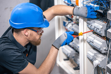 A male electrician works in a switchboard with an electrical connecting cable.