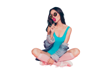 Full size lady sit on floor with her wave brunette hair she eat sugar sweet caramel sucker on stick wear in style spectacles stockings casual denim jeans shirt isolated on pink background