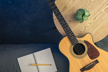 Acoustic guitar and notepad with pencil on the table, top view.