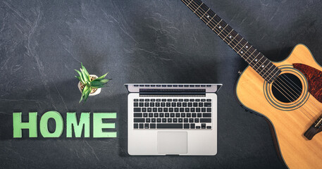 Acoustic guitar, laptop and decorative word Home on a dark background, top view.