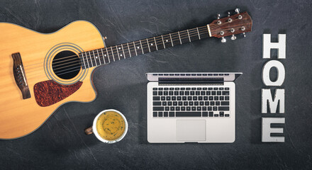 Laptop, acoustic guitar and a cup of tea on a black background, top view.