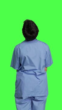 Back view Stressed nurse being in a hurry with the checkup appointments, waiting for patients to arrive at examinations. Medical assistant with scrubs acting impatient against greenscreen backdrop