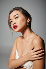 portrait of attractive asian woman holding to shoulder and looking to up on grey background