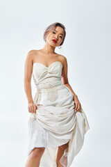 graceful asian woman in white elegant outfit with red lips tilted head and lifted her dress