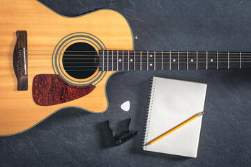 Acoustic guitar and notebook on a black textured background, top view.