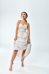attractive asian woman in white elegant outfit with red lips lifted her dress and looked to side