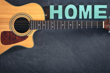Acoustic guitar and decorative word Home on a textured black background.