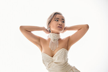 graceful asian woman in stylish necklace looking to side and putting hands behind head