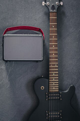Electric guitar and speaker on a textured black background, top view.
