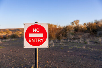 No entry sign with a desert landscape out of focus in the background.  Copy space on the right of...