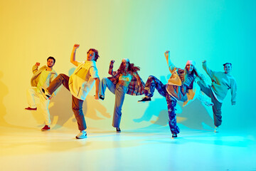 Young men and women in motion, friends in dynamic poses dancing against gradient green yellow background in neon light. Concept of modern dance style, hobby, active lifestyle, youth culture