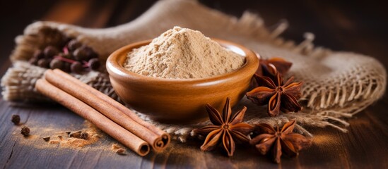 A bowl of cinnamon powder alongside cinnamon sticks and star anise on a wooden table, ready to be used as ingredients in a delicious recipe
