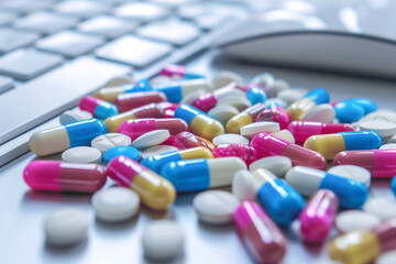 Multicolored pills on a white desk with computer keyboard and mouse in the background. 