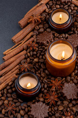Soy scented candle in a jar. Coffee beans, anise, cinnamon spices. The candles are burning. Dark...