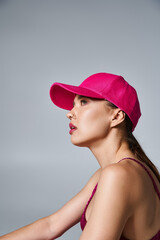 Side view of beautiful brunette woman in trendy attire and pink cap in studio setting