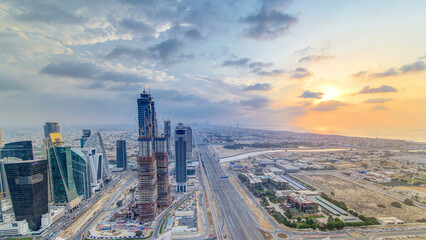 Dubai business bay towers with sunset timelapse. Rooftop view of some skyscrapers and new towers under construction. - obrazy, fototapety, plakaty