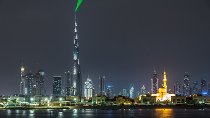 Modern Dubai city skyline timelapse at night with illuminated skyscrapers over water surface