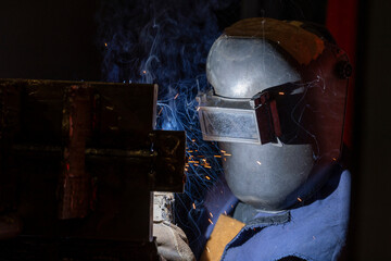 A masked worker is fully immersed in their welding task. Bright sparks fly as they focus intently on a specific point of the metal. 