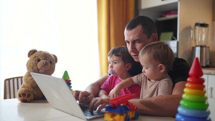 father working from home a remotely with two baby in fun his arms. pandemic remote work business concept. father tries to work at home in kitchen, baby children interfere sitting on their hands - 767105953