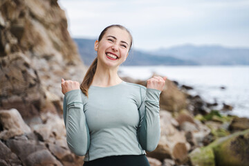 Fototapeta na wymiar Young woman in sporty wear win competition raising fists celebrating cool achievement, cheerful positive girl all possible yelling voice raised fists in delight emotional high spirits mood