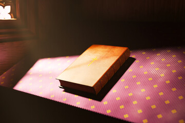 Closed Hardcover Book with Golden Cross on Purple Cloth in Dim Light
