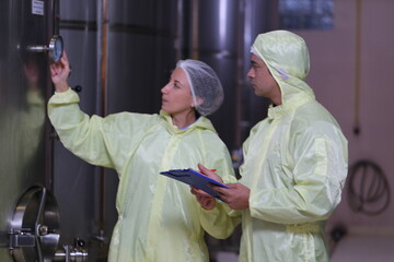 Winemaker woman and business owner wearing a sterile suit working and inspecting wine tanks in a...