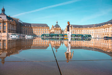 Adult man walking with the city palace of Bordeaux with a symmetric reflection on a mirror of water.
