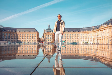 Adult man walking with  the city palace of Bordeaux with a symmetric reflection on a mirror of...