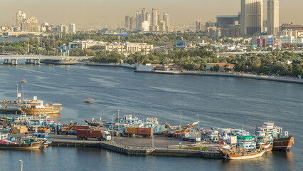 Fototapeta premium Dubai creek landscape timelapse with boats and ship in port and modern buildings in the background during sunset