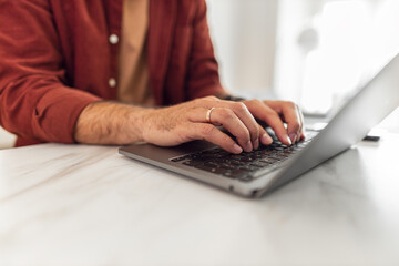 A close-up shot of man's hands typing on a laptop while working from home