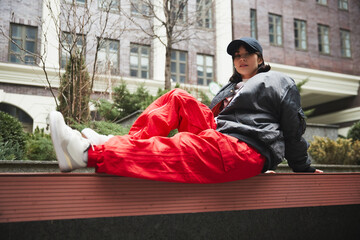 Contemporary urban clothing outlets. Stylish beautiful young woman sitting on bench in red cargo...