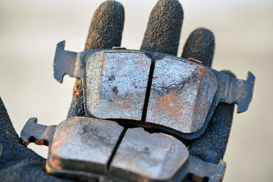 Uneven brake pads wear, used brake pads in mechanic hands. Uneven brake pad wear caused problem with the caliper. Car maintenance. Selective focus.
