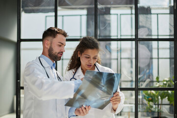 Young serious competent male doctor looking at X-ray at doctor's office