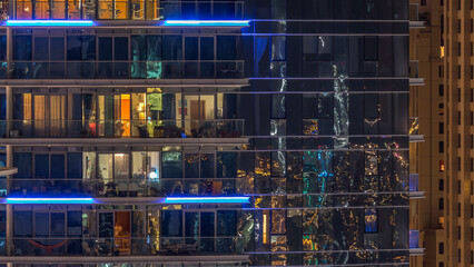 Glowing windows in multistory modern glass and metal residential building light up at night...