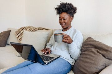 Happy African American woman having fun using laptop at home. Laughing watching funny online videos.