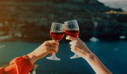 Women clink glasses of red wine against the backdrop of the sea. - 767149723
