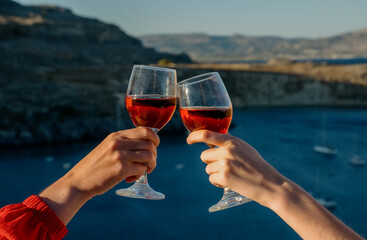 Women clink glasses of red wine against the backdrop of the sea. - 767149738