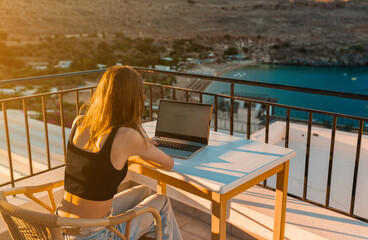 A young girl works on a laptop on the balcony at sunset. - 767149777