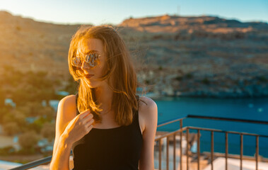 A girl in sunglasses stands on the balcony. Vacation concept. - 767149781