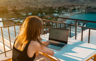 A young girl works on a laptop on the balcony at sunset. - 767149791