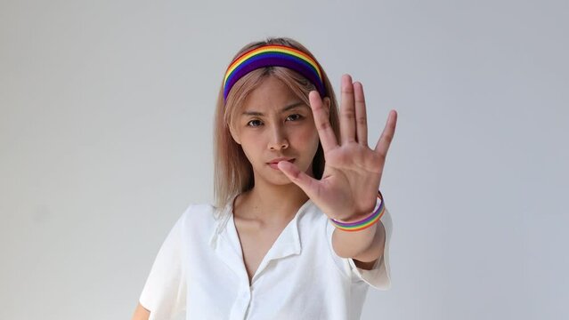 Unhappy LGBT Woman Wearing Rainbow Wristband and Headband showing stop hand sign