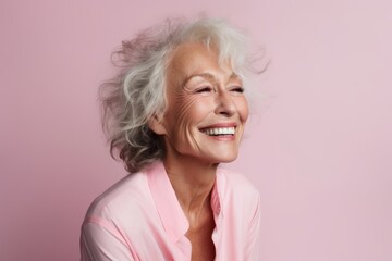 Portrait of happy senior woman laughing and looking at camera against pink background