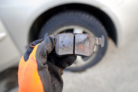 Mechanic holds bad brake pad in hand, replacing worn uneven defective pads. Vehicle brake system service, brake pad replacement. Car maintenance. Selective focus