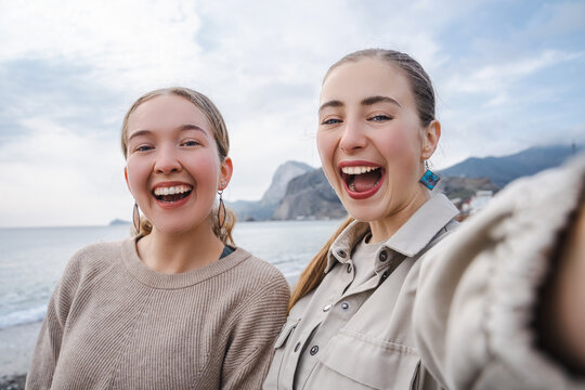 Happy joyful tourist girls are smiling at the camera, female friends taking selfie self portrait photos on smartphone at the beach, hipster girls having fun, showing positive face emotions