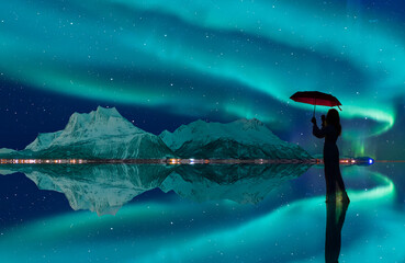 Northern lights in the sky over Tromso, Norway - Young girl in white dress holding red umbrella and walking on the calm water