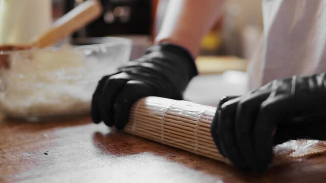 Woman in black gloves prepare sushi rolls home in kitchen, skillfully rolling them up . Concept homemade sushi-making, culinary craftsmanship  joy of creating delicious dishes.