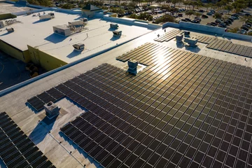 Fotobehang Production of sustainable energy. Aerial view of solar power plant with blue photovoltaic panels mounted on industrial building roof for producing green ecological electricity © bilanol