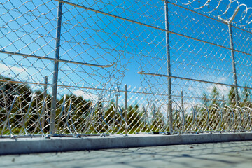 Damaged Metallic Chain-Link Fence with Razor Wire Against a Clear Blue Sky