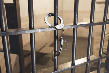Close-up View of Handcuffs Hanging on Cold Iron Bars of a Dark Prison Cell